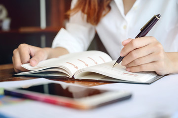 Closeup image female hand holding pen and writing on diary.