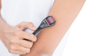 Close up of woman’s hand using derma roller on islolated white background, derma roller in focus....