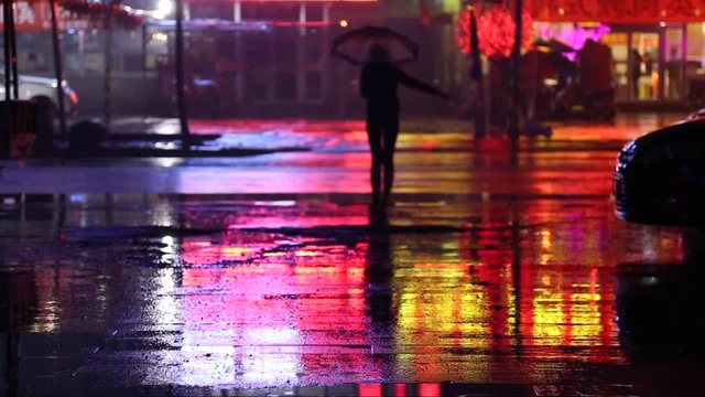 Cinemagraph of a woman in the evening on a road staying still with an umbrella while it is raining. Reflections moves