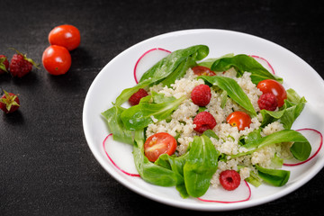 Quinoa salad with vegetables, raspberry and tomatoes on the black table. Super food for healthy and concept of balanced diet