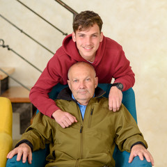 Senior father and young smiling son looking away in a home. Happy old man grandfather looking away...