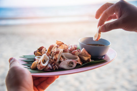 Grilled squid on beach sea background / Slice of squid on plate with thai seafood sauce