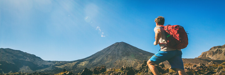 Hiker man hiking in banner landscape Tongariro National Park Alpine crossing hike trail man tramper tramping panoramic. North Island. Adventure travel traveler walking trek with bag backpacking. - obrazy, fototapety, plakaty