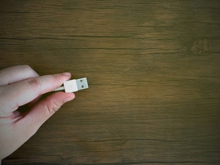 Woman left hand holding USB cable for connect with electronic part on wooden table.
