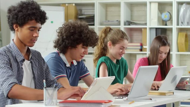 Lockdown of four students sitting at desk and using devices for studying
