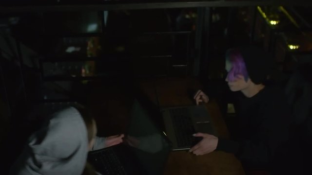 High angle view of two young Caucasian women in hoodie sitting down at table in front of each other, putting laptops on it and starting typing on keyboards