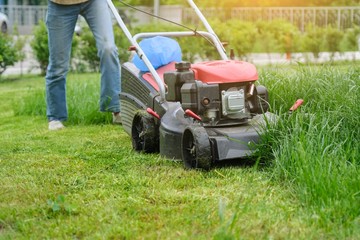 Gardener woman legs mowing grass with lawnmower, city courtyard of an apartment building