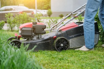 Gardener woman legs mowing grass with lawnmower, city courtyard of an apartment building