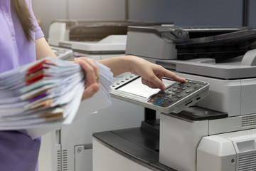 Bussinesswoman using copier machine to copy heap of paperwork in office. - obrazy, fototapety, plakaty