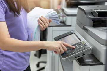 Bussinesswoman using copier machine to copy heap of paperwork in office.