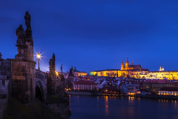 Looking along the Charles Bridge toward the illuminated St. Vitus Cathedral and Prague Castle at twilight