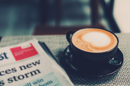 A cup of coffee and a newspaper of coffee on a wooden table