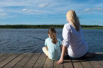 Fototapeta premium woman with her daughter is fishing on the pier in sunny weather, rear view