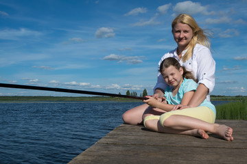 Fototapeta na wymiar mother and daughter are resting on the pier of a beautiful lake