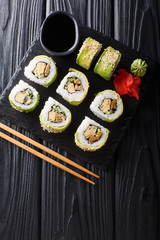 Japanese rolls wrapped in avocado with omelet, sesame and cucumber closeup on a plate. Vertical top view