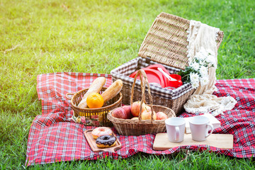 Picnic basket with fruit and bakery on red cloth in garden.