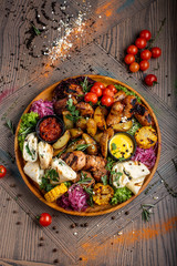 Fototapeta na wymiar Tasty dish with meat and vegetables, baked pork, cowboy grill, grilled potatoes with sauce. Assorted tasty grilled meat with vegetables and herbs