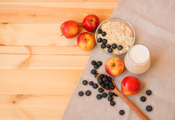 Glass of yogurt, apples and oat flakes in bowl with blueberries on wooden table.