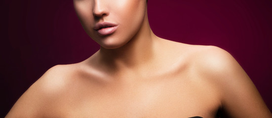 Lips, part of face, shoulders of young woman with perfect skin, nude makeup. Dark red background