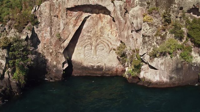 Drone shot of a large Maori rock carving on blue water