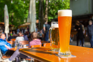 A wheat beer and a pils are standing on a table in a beer garden