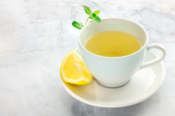 Obraz na płótnie Canvas A cup of green tea with a wedge of lemon and mint leaves, with a place for text