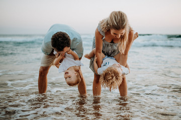 A young family with two toddler children having fun on beach on summer holiday.