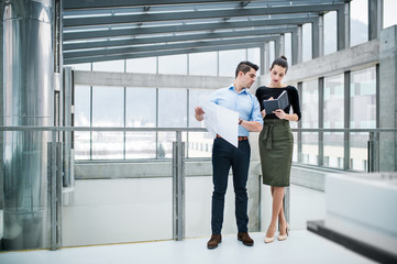 Two young architects with blueprints standing in office, talking.