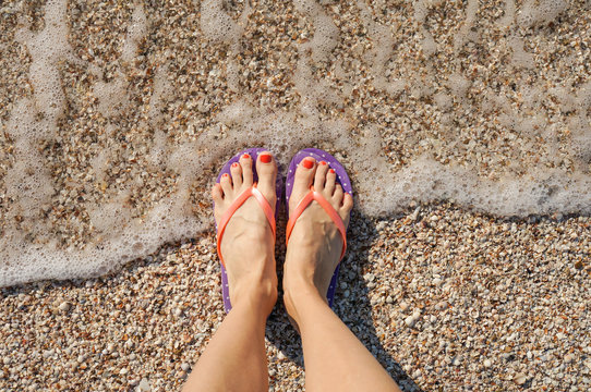 Funny woman legs enjoying her summer vacation wearing flip flops standing near seaside