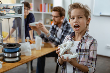 Excited little boy in checkered shirt playing with model of dinosaurs