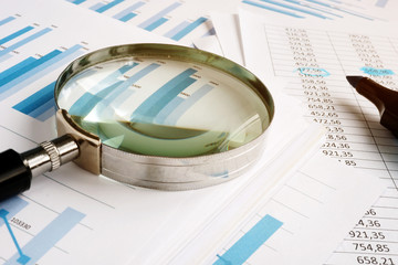 Magnifying glass for audit and stack of business reports.
