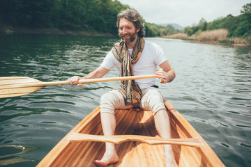 Cheerful canoeist paddling wooden boat. Smiling bearded guy with wooden paddle on a canoe