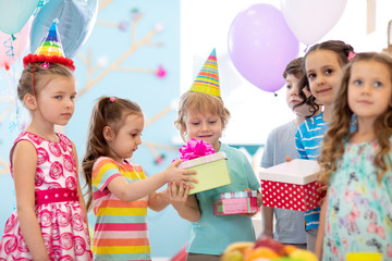 Childhood, holidays, celebration, friendship and people concept. Happy children in party hats giving gifts at birthday party
