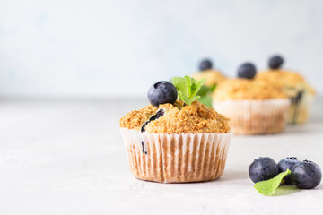 Blueberry muffins with fresh berries and mint leaves on light grey stone background. Copy space.