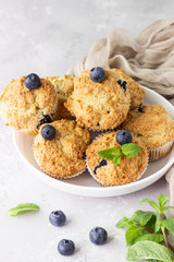 Blueberry muffins with fresh berries and mint leaves on light grey stone background. Copy space.