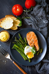 Salmon fish steak grilled with asparagus, poached egg on black background. Healthy food. Top view flat lay.