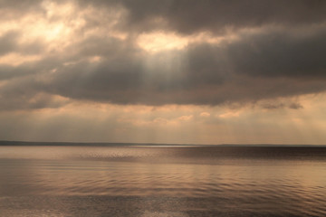 Fototapeta na wymiar Sunrays through clouds over the still lake before the rain