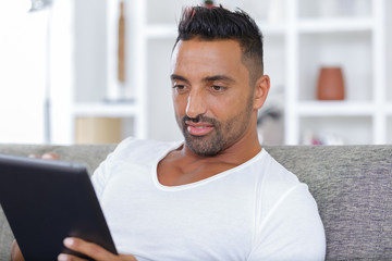 man with tablet pc computer sitting on sofa at home