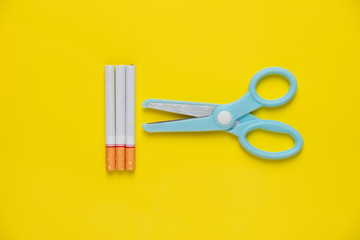 Blue scissors cut cigarette and tobacco on yellow background pastel tone. quitting smoking for...