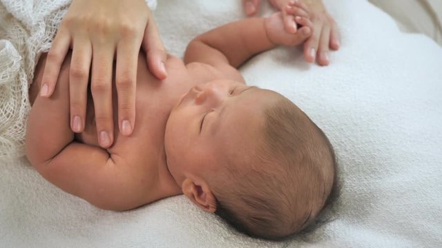 Close up of mother hands lulling newborn baby on bed at home