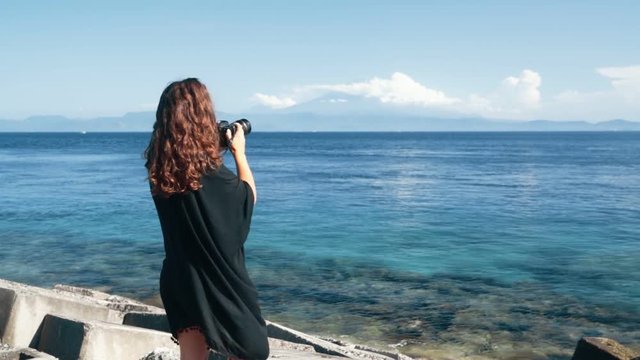 Back side view of girl photographer takes pictures of ocean, mountains, slow motion