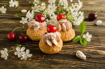 Choux Buns with Craquelin (crispy cream puffs) filled with cherry cream decorated with fresh cherry, cherry flowers and almonds on wooden background