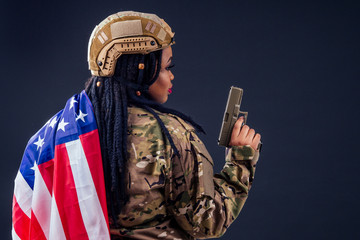 Fototapeta na wymiar afro american army latin soldier in camouflage clothes hair dreadlocks evening makeup and big lips holding a weapon on black background in studio with american flag,independence day usa 4th of july