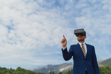 Businessman uses VR-headset to display a virtual reality on a background of blue sky and mountains