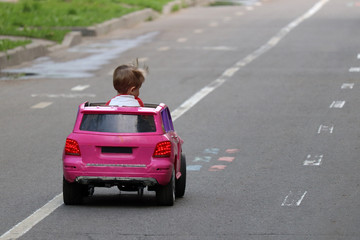 Little boy driving big toy car on a road. Kid playing outdoors in summer, concept of learning driving, novice driver