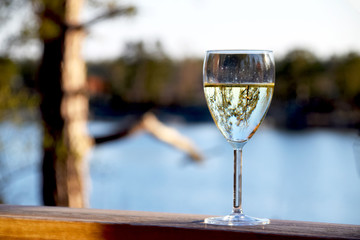 Glass of white wine on wooden deck railing with a beautiful view of the sea in the background on a summer evening in Sweden