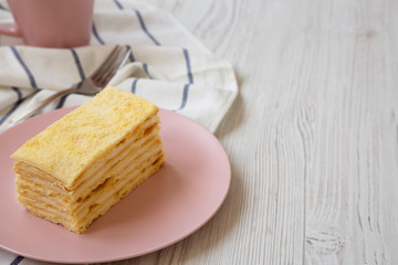 Piece of Napoleon Cake on a pink plate over white wooden background, side view. Copy space.