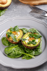 Quail eggs baked in avocado. Avocado egg boats served with spinach leaves on gray plate. Ketogenic, keto low carb diet.