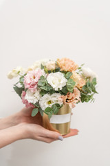 Beautiful floral arrangement of mixed flowers in woman hand. Golden flowerpot. The work of the florist at a flower shop. Delicate Pastel color. Fresh cut flower.