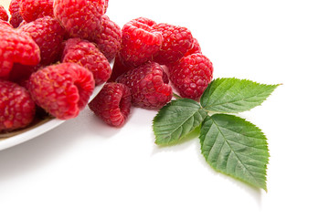 Small plate with ripe raspberries and green leaf isolated on white background.